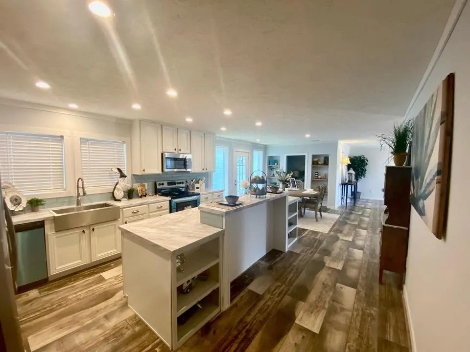 Open white kitchen with farmhouse sink, island, and wood-look floors
