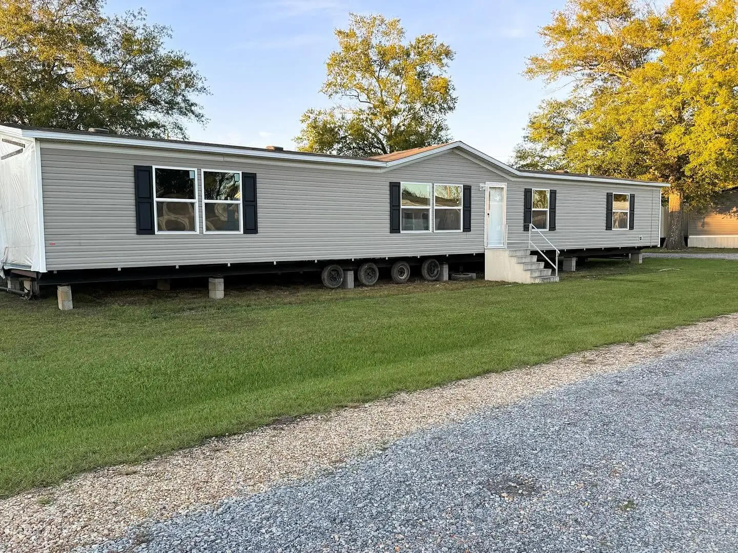 A gray double-section home with black shutters on the Southern Colonel lot at golden hour